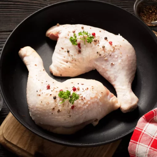 Deux cuisses de poulet posées dans une assiette creuse noire avec une serviette à carreaux rouge et blanc