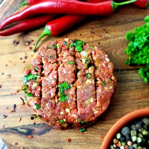 Un steak de kefta (viande épicée) sur un plateau avec épice, piment rouge et persil